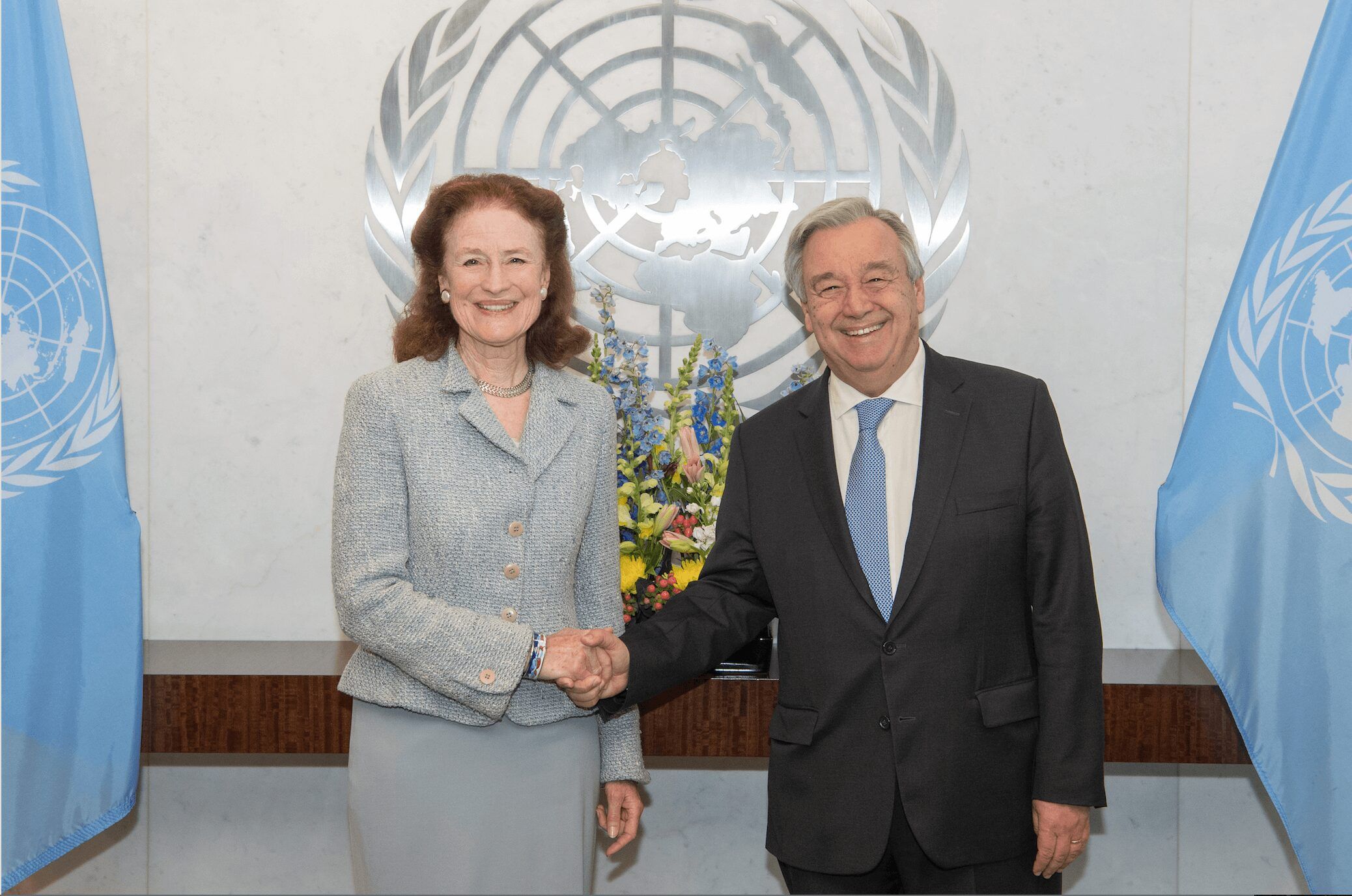 Man and woman shaking hands in front of UN emblem