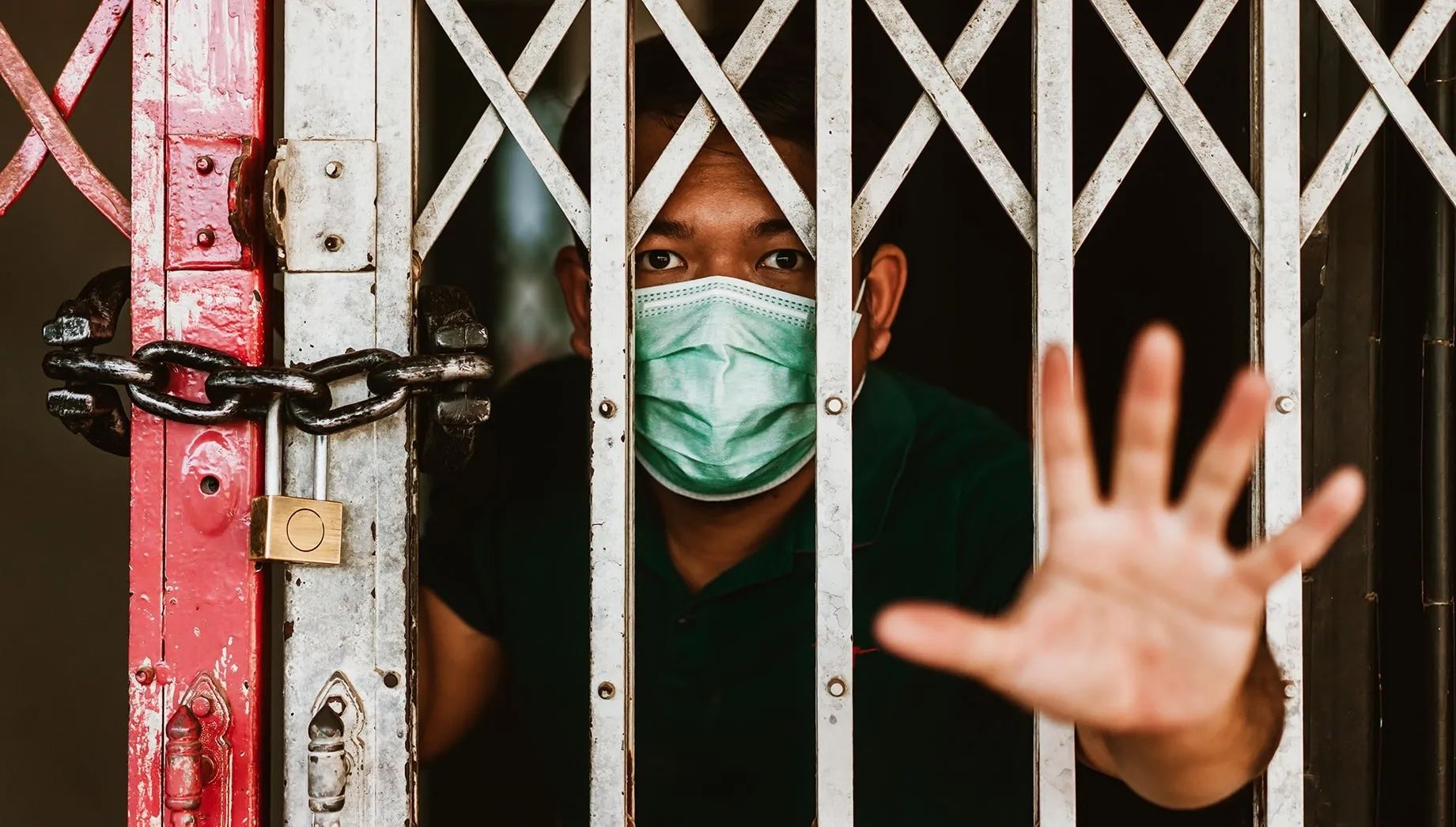 Person in a mask behind a gate holding their hand out.