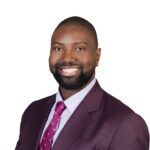 Headshot of a person wearing a purple suit and red tie with white background.