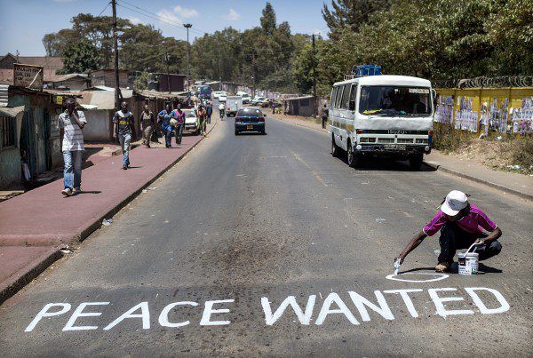 Woman paints Peace Wanted on street in third world country