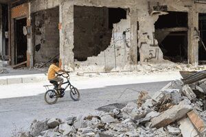 Boy riding bike down a destroyed street