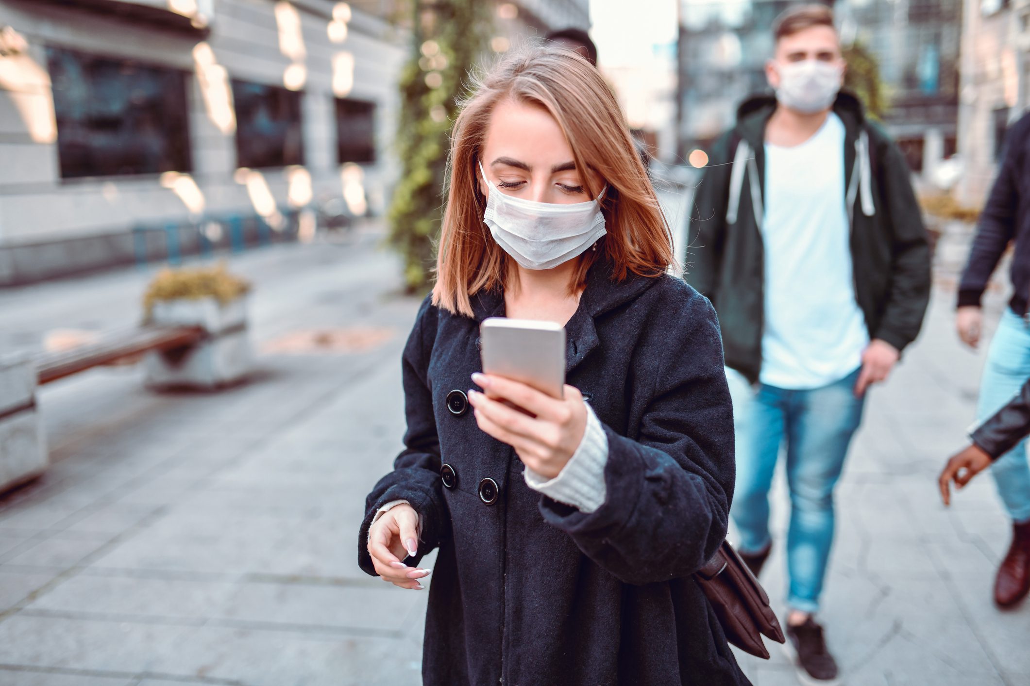 Female Using Smartphone Among Many People Walking With Face Masks Through City