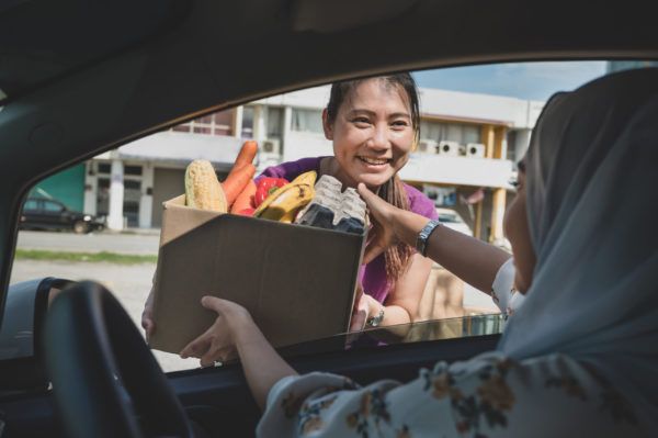 A female volunteer hand out free food to car driver during a drive through food bank charity campaign in early morning.