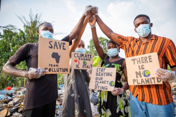 Four young adults protest with signs against pollution outside an illegal open landfill in Africa