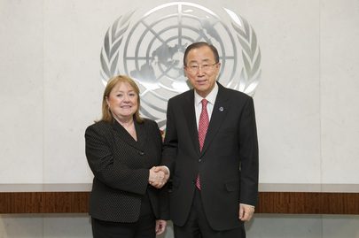Man and woman shake hands in front of UN emblem