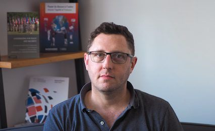 Headshot of a person wearing glasses, with a bookshelf in the background