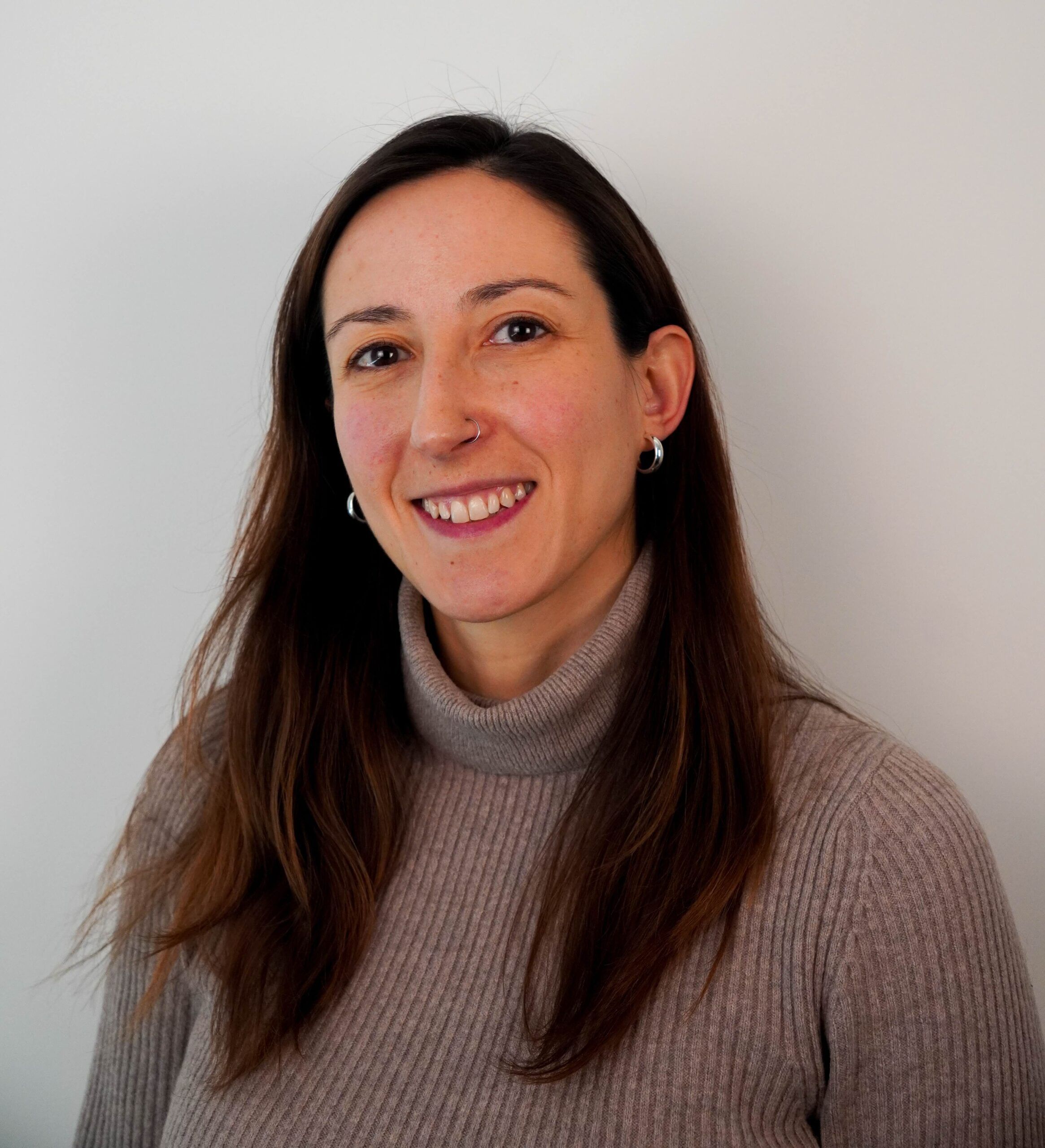 Headshot of a person with long brown hair and a turtleneck top smiling against a white background.