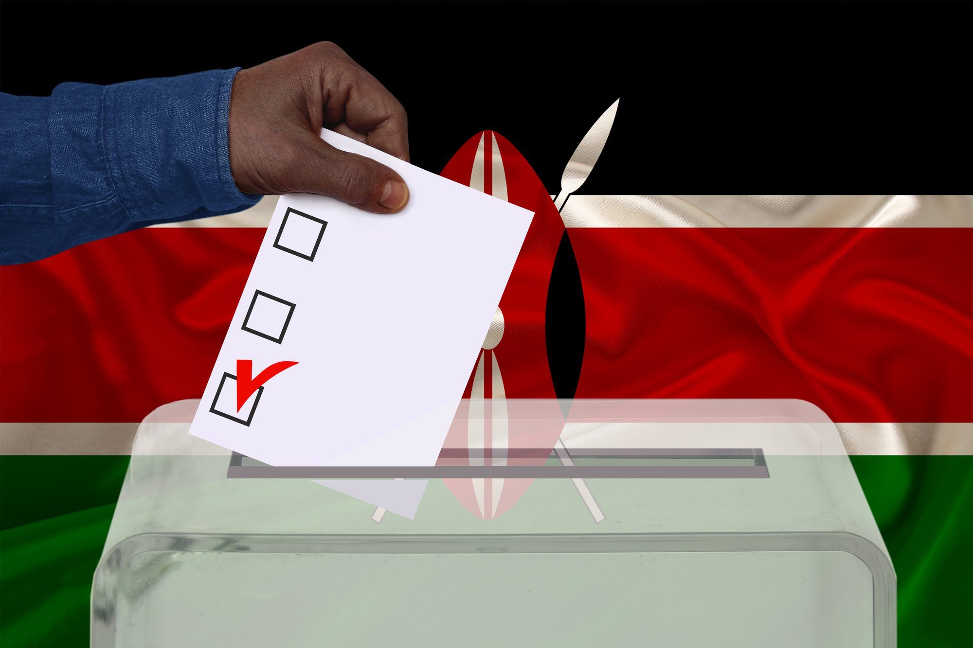 Male voter drops a ballot in a transparent ballot box against the background of the Kenya national flag