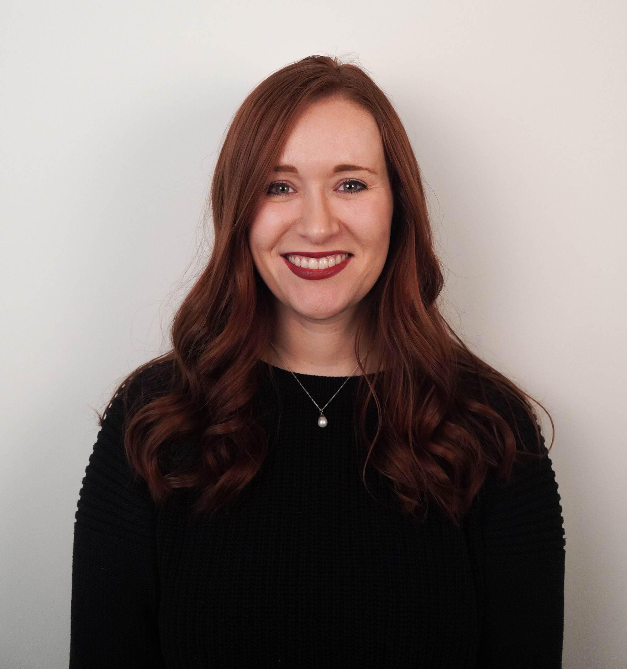 Headshot of a person with red hair and a black top against a white background.