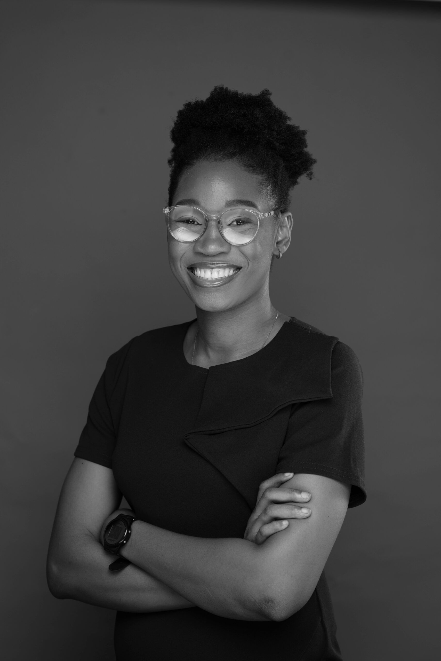 Black and white shot of Kelechi Achinonu, a young woman wearing glasses and a black t-shirt, with arms crossed