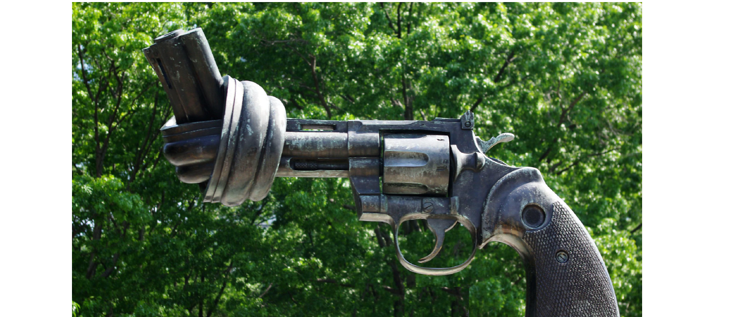 Knotted gun statue in front of greenery.