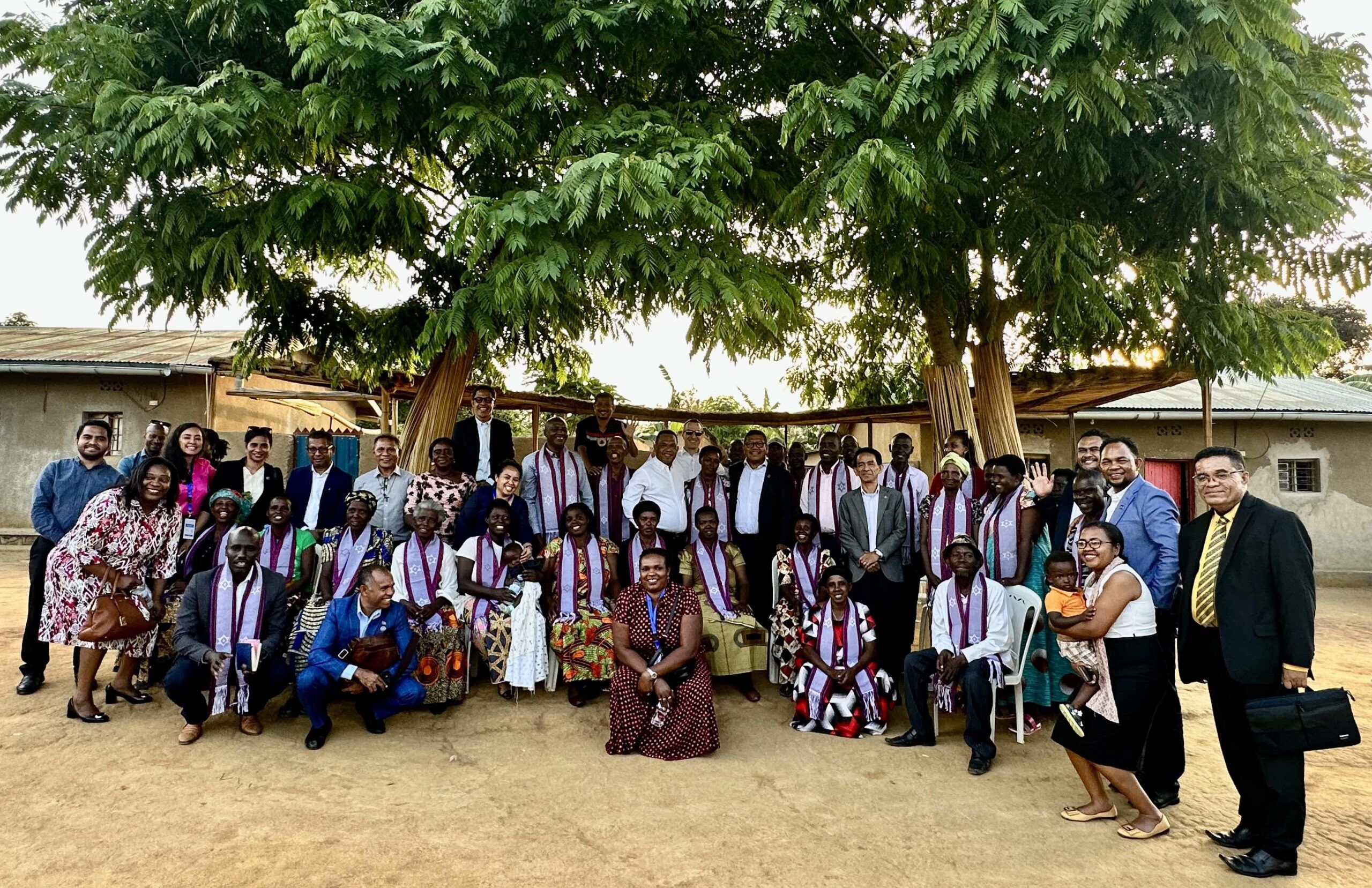 Large group photo at a Rwanda Reconciliation Village standing in front of trees outside.