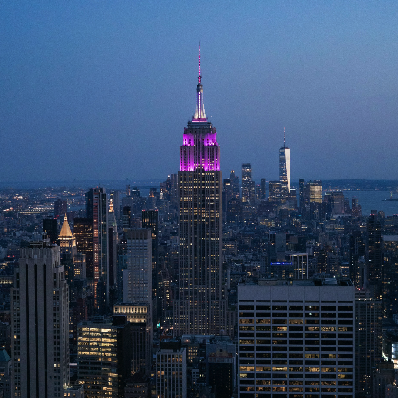 New York City skyline at night. The Empire State Building is lit up with the NYU purple color.