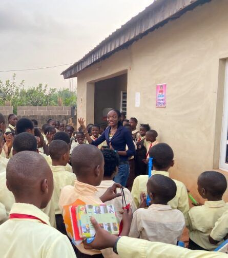 Group of school children looking at the facilitator in front of a schoolhouse.