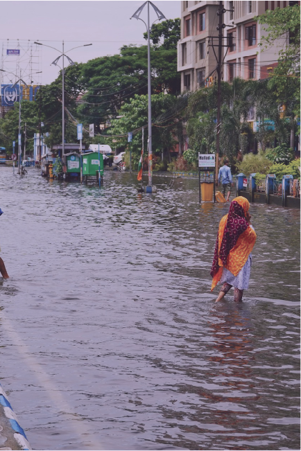 Flooded street in India with a woman walking across with hills and buildings in the background.