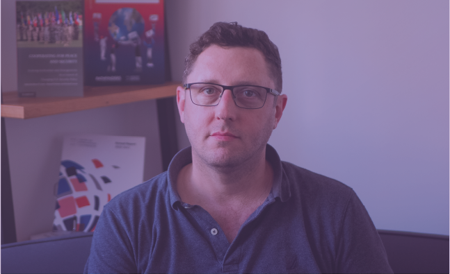 Photo of a person with glasses and collared shirt with purple fade over the photo