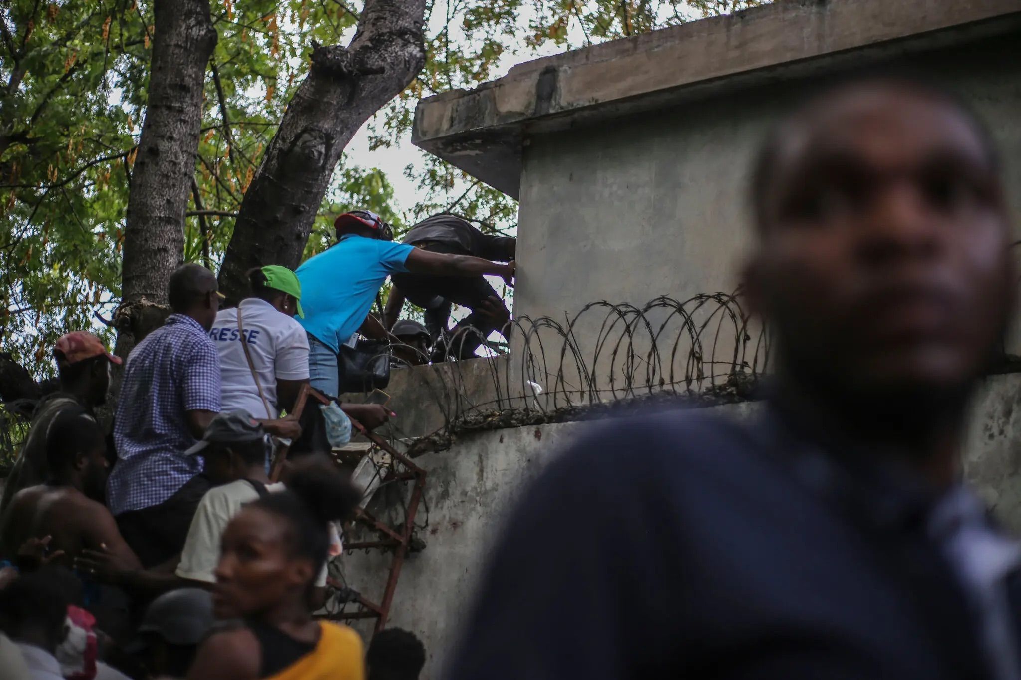 Journalists climb a wall to take cover from gunfire after being shot at by armed gangs at the General Hospital in Port-au-Prince.Credit...