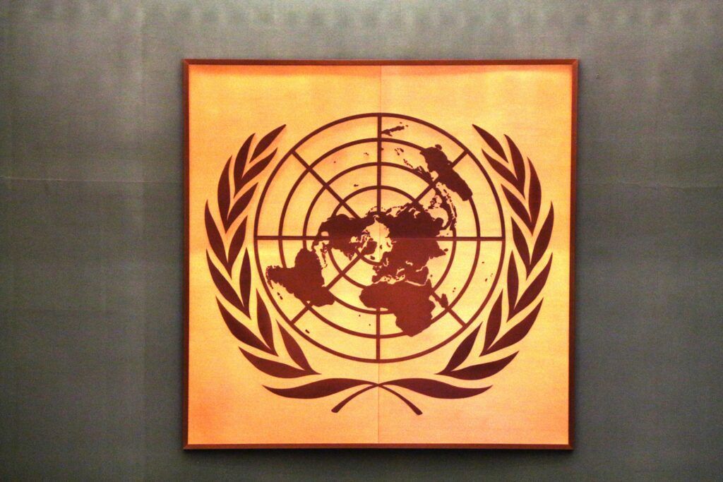 Painting of the UN logo in black on a square/orange frame.