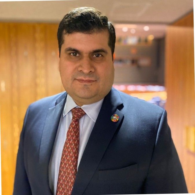 Photo of a person in a blue suit and red tie.