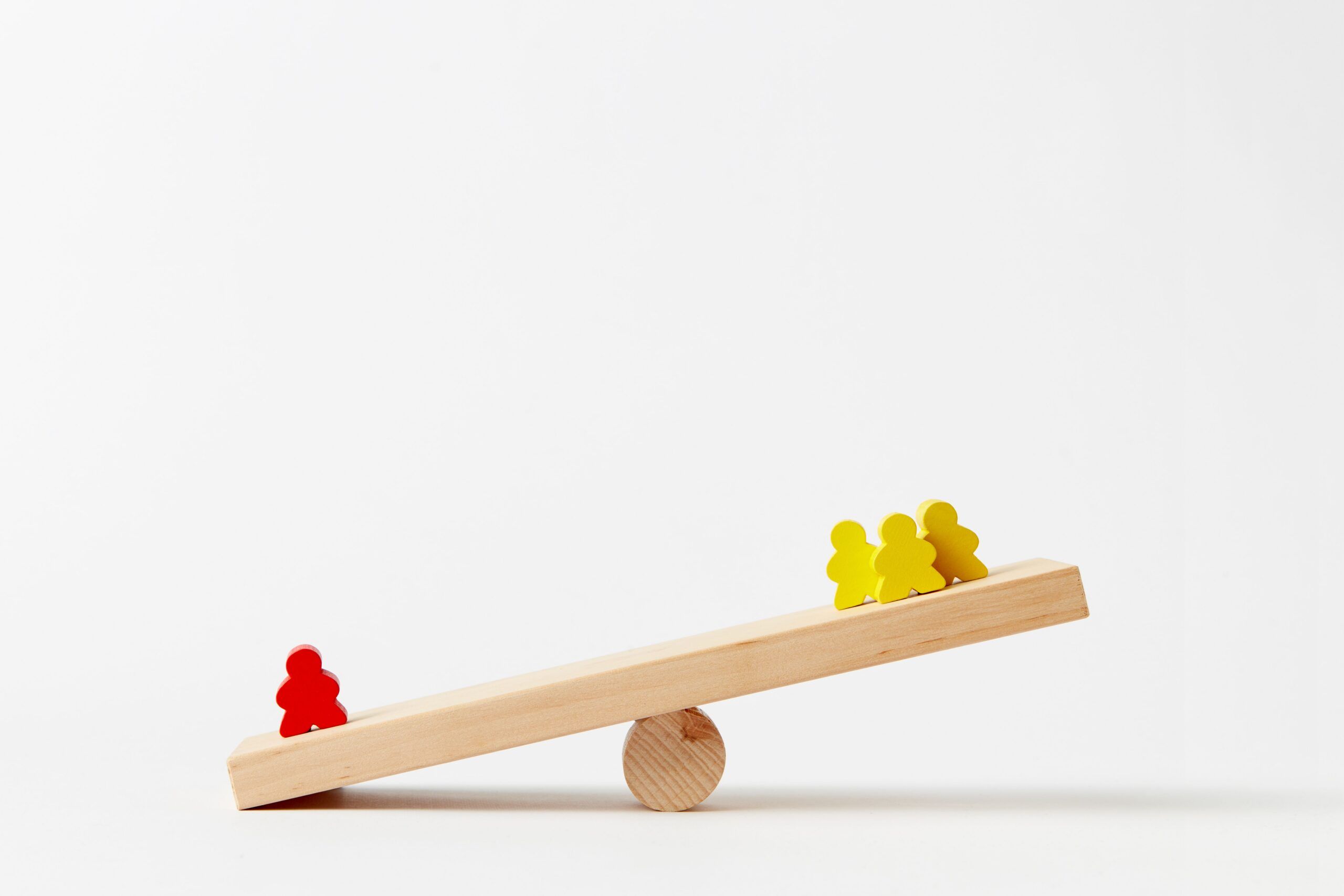 Wooden blocks on a seesaw. Bottom left is a single red person. Top right is a few yellow blocks.
