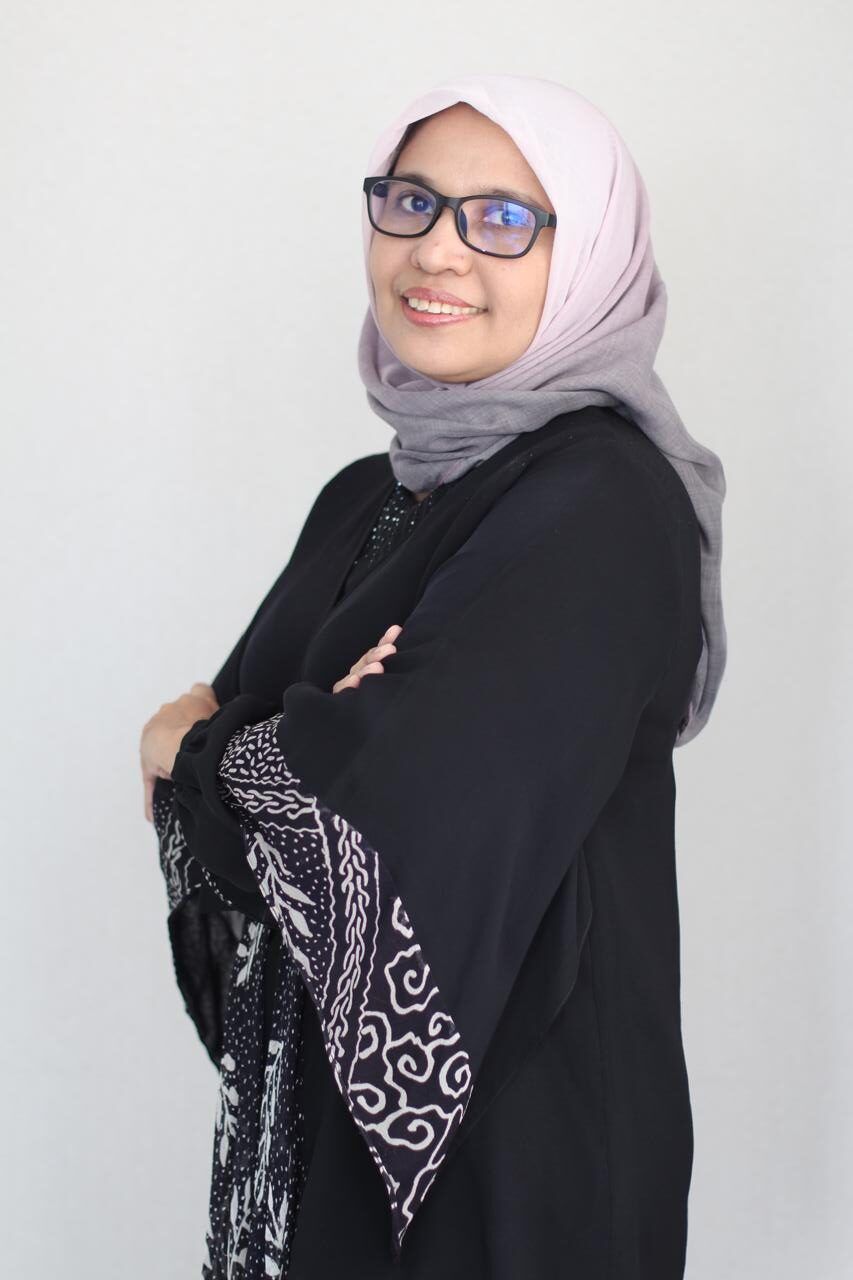 Headshot of a person wearing a white headscarf, glasses, and a black dress.