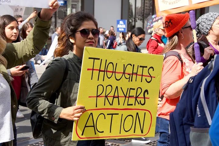 Person holding up a yellow sign with thoughts and prayed crossed out, but action is circled.