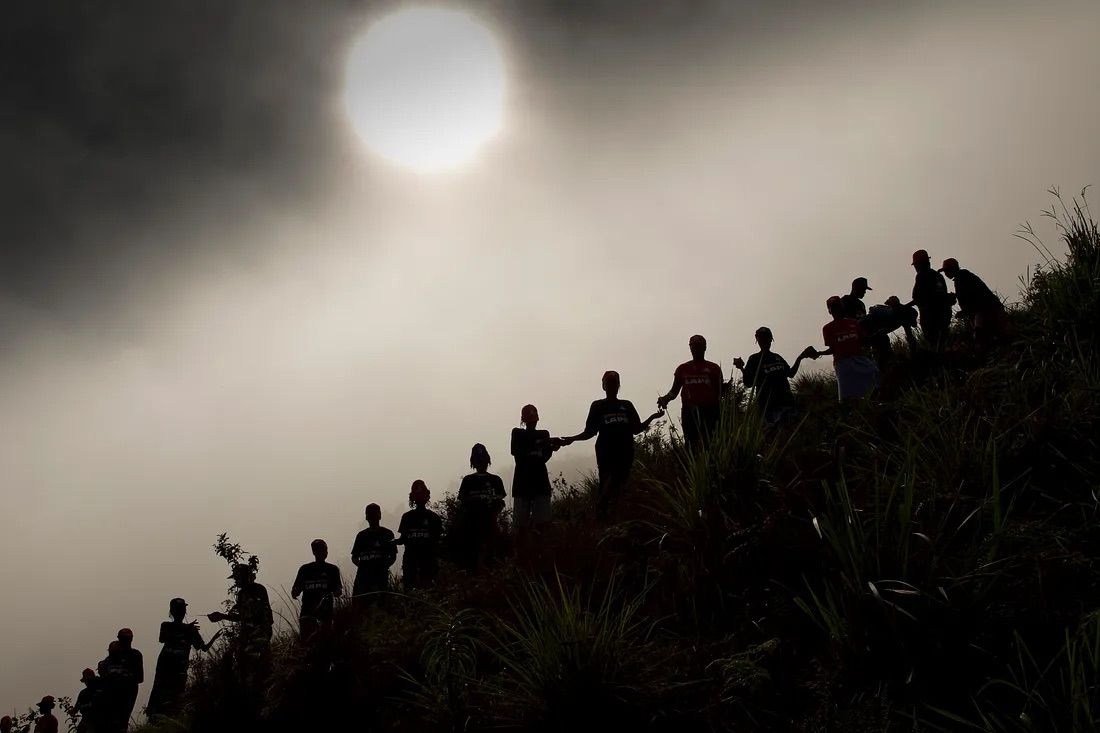 Silhouettes of people in a line on a slanted hill.