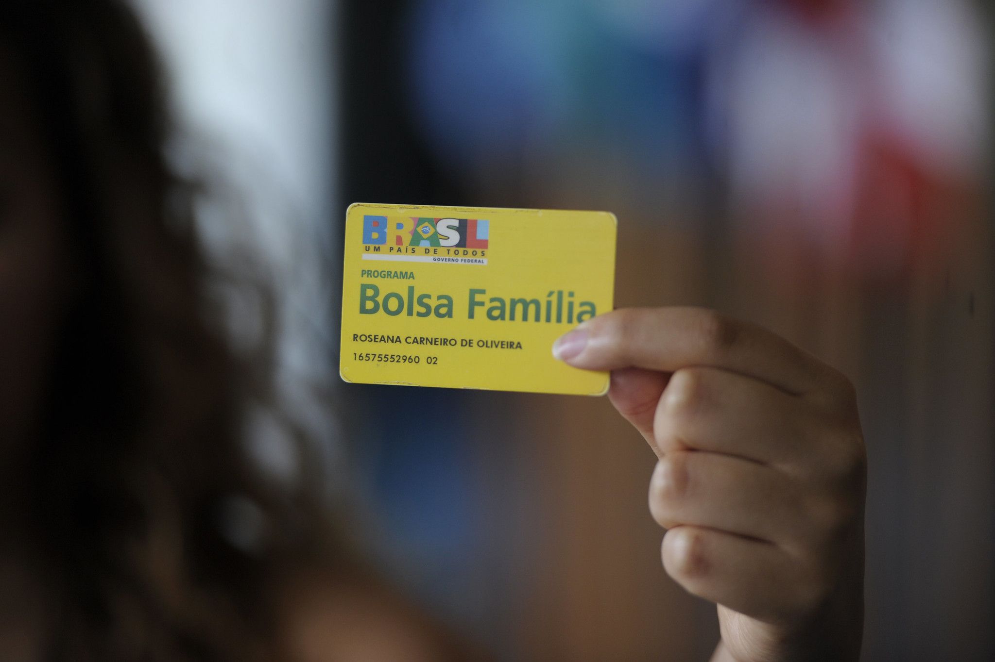 Hand holding a "Bolsa Família" yellow card.