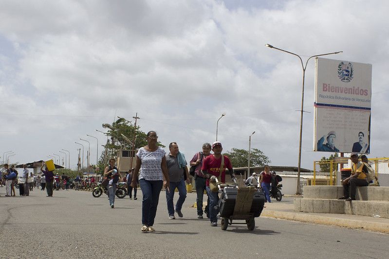 People walking on a road, with one person holding a hand truck. In the distance there is a faded sign on the right with 