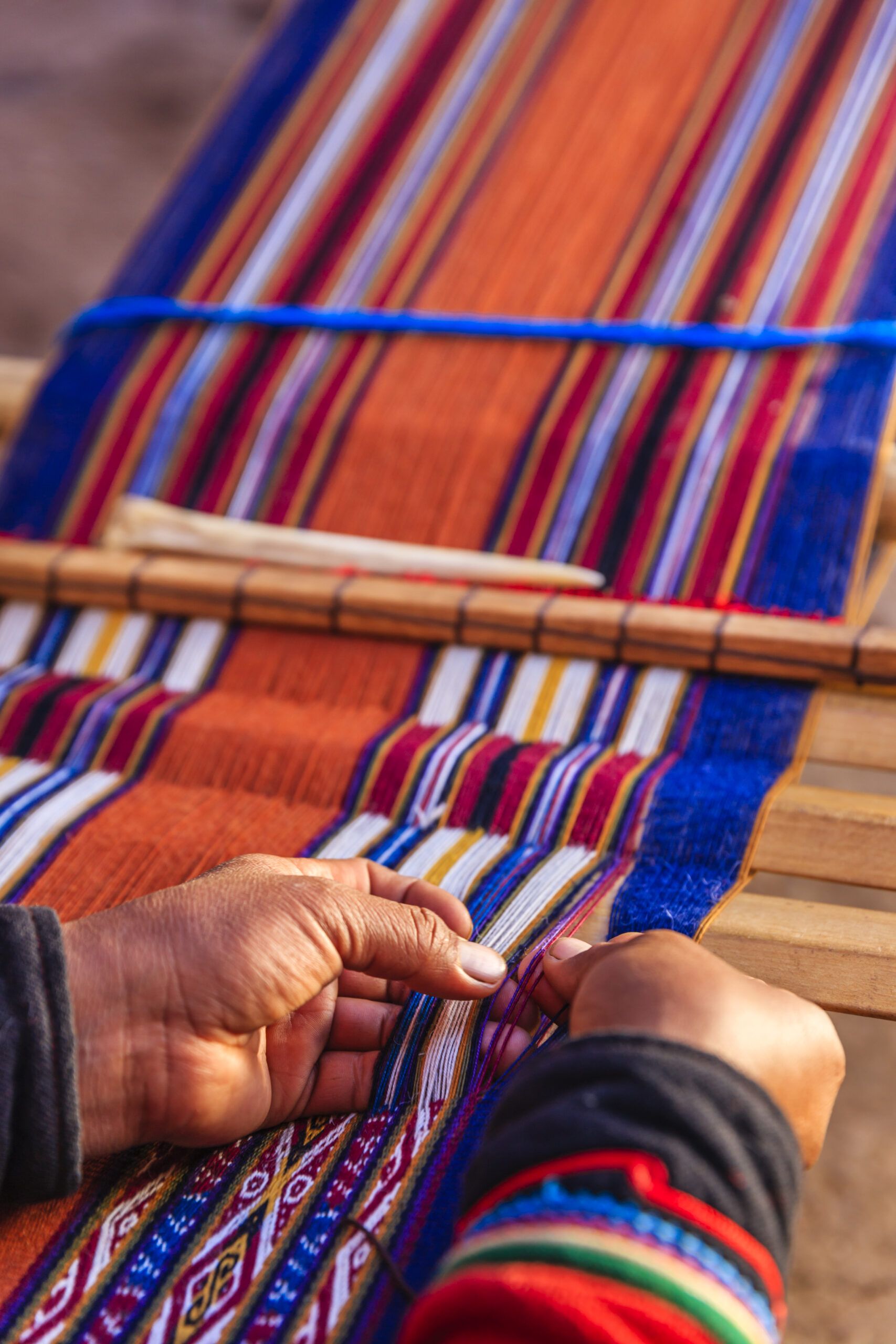 Hands weaving at a loom, with colorful fabric in the loom.