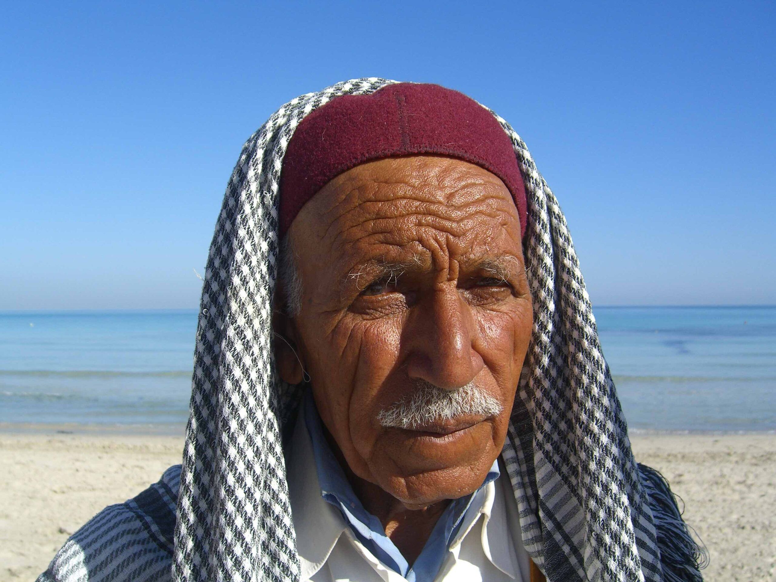 Man with a mustache wearing a head scarf in the desert.