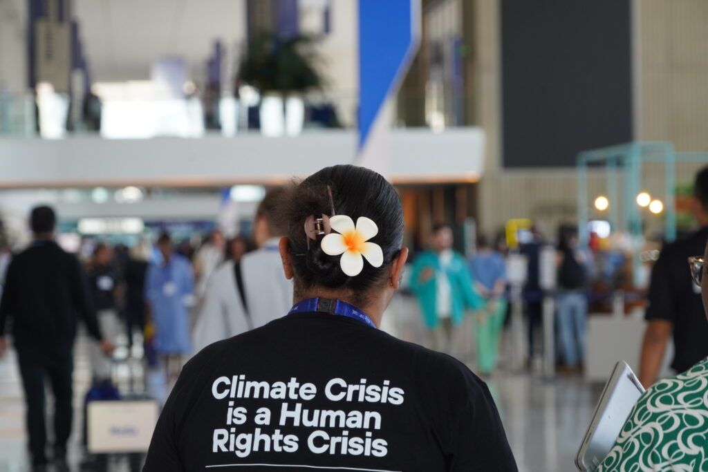 Back of a woman with a flower in her hair. Her shirt says the text: "Climate Crisis is a Human Rights Crisis."