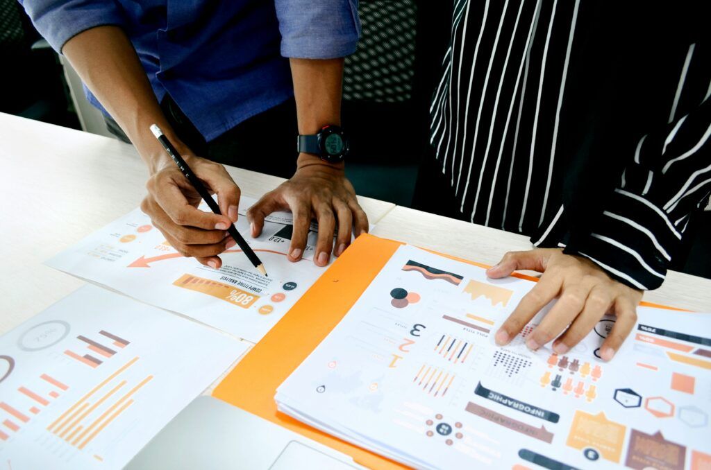 Two sets of hands writing on a table full of charts.