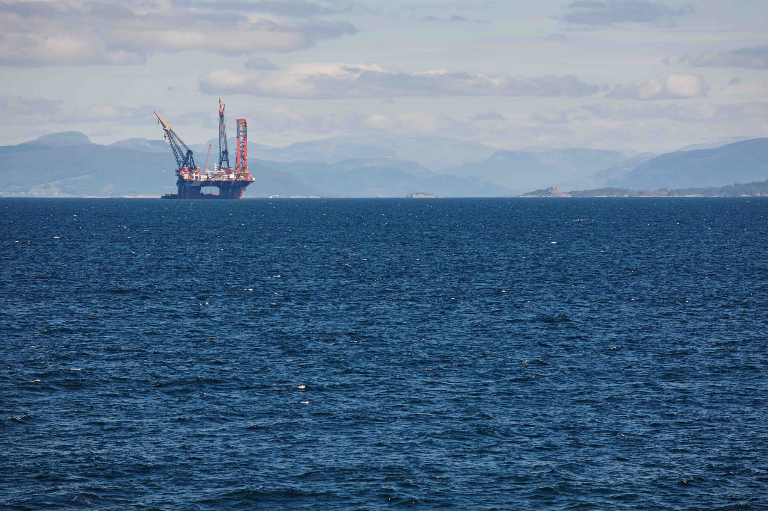Oil and gas sea platform in the distance of a large body of water. Mountains and cloudy sky background.