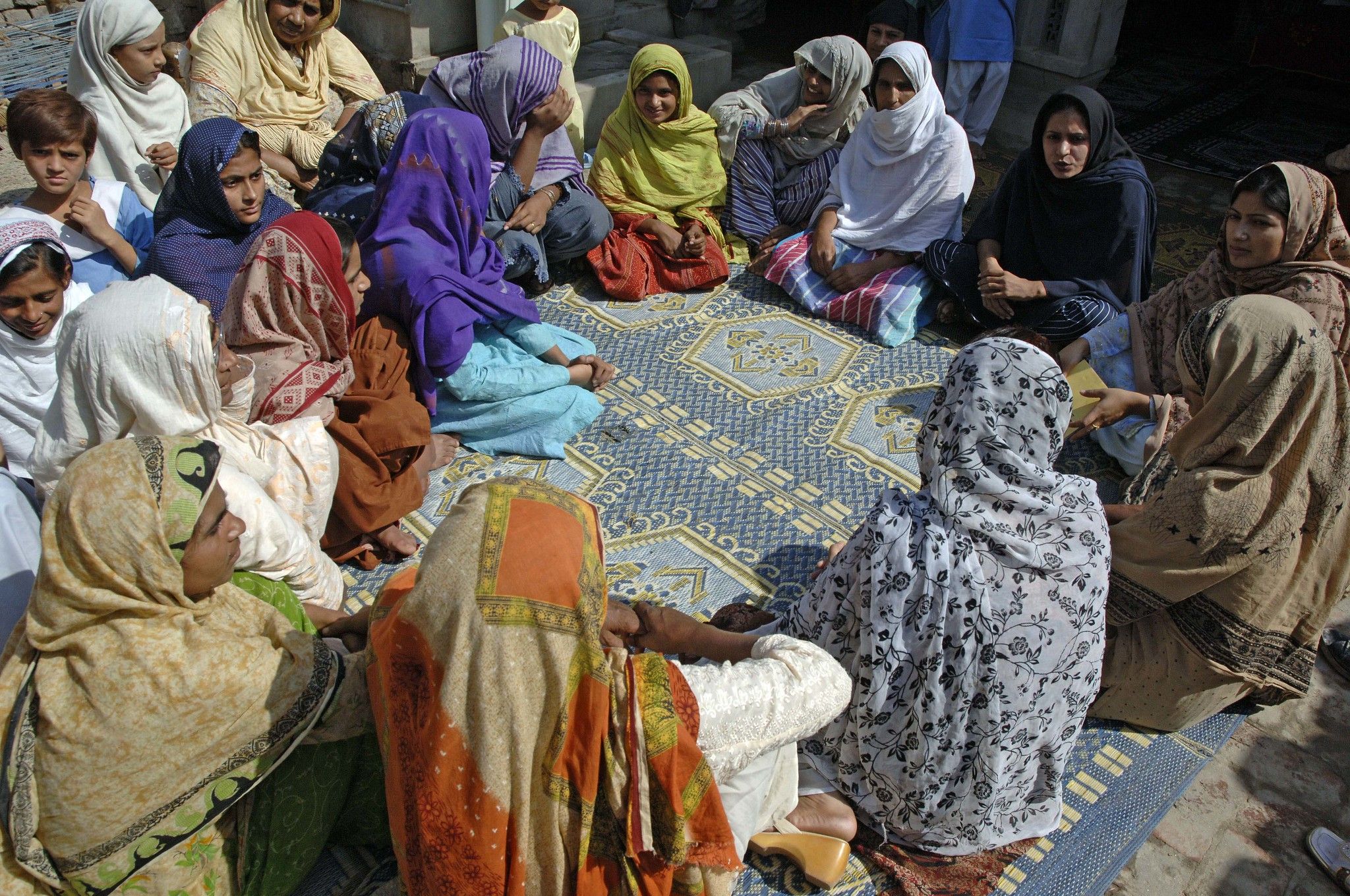 Group of women with headscarves gathered around in a circle.