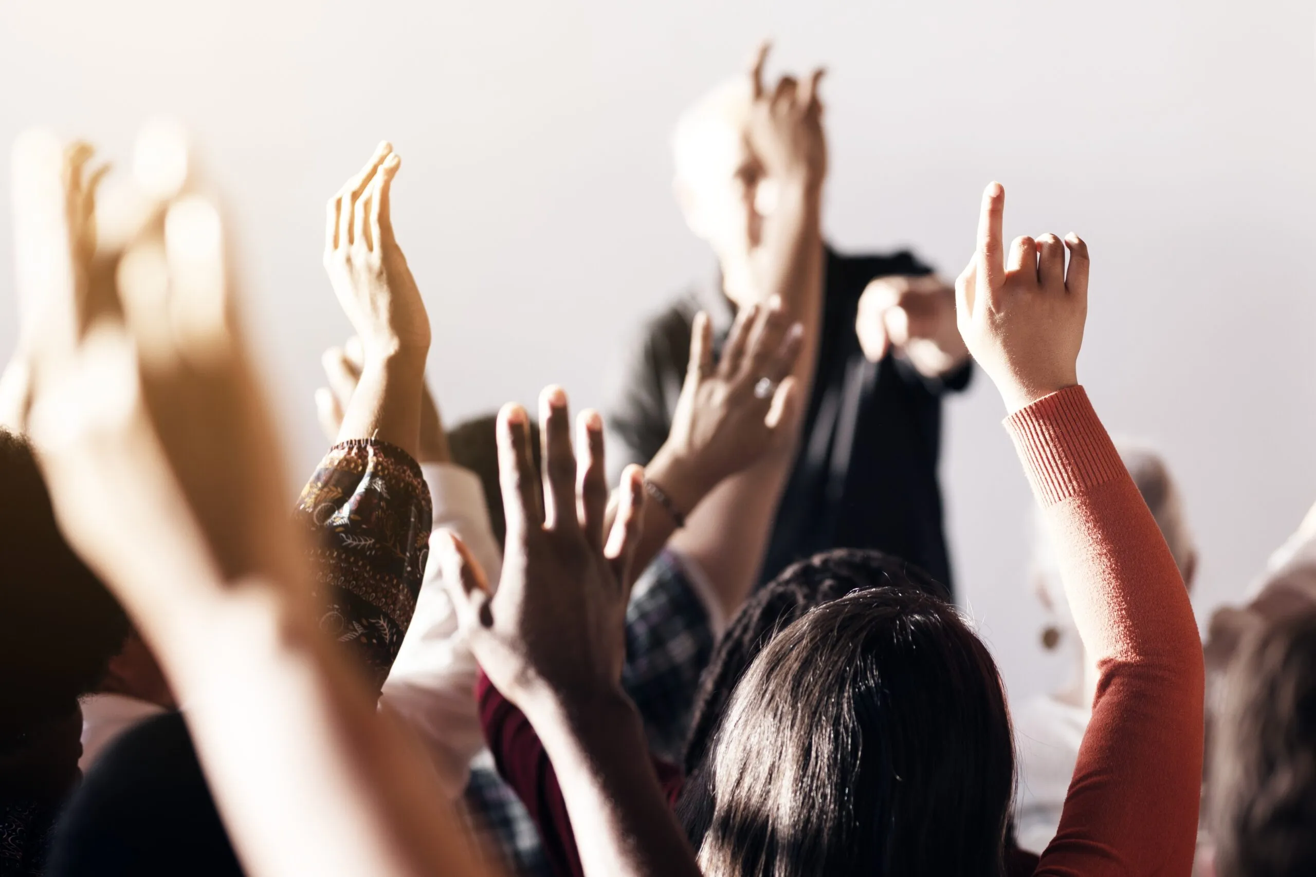 A diverse group of people raising hands in a classroom or seminar setting, with a focus on participation and engagement.
