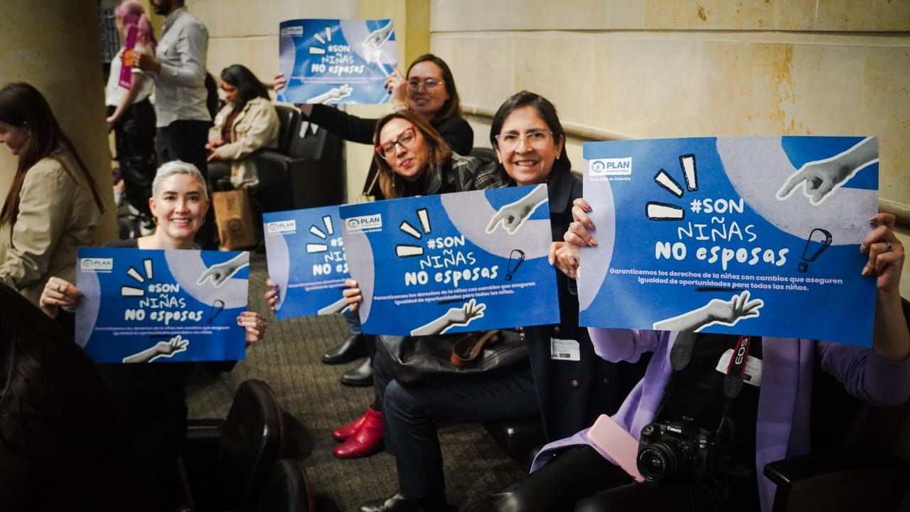 Three Plan International Colombia staff members holding up signs to show support for the bill to eliminate child marriage in a room.