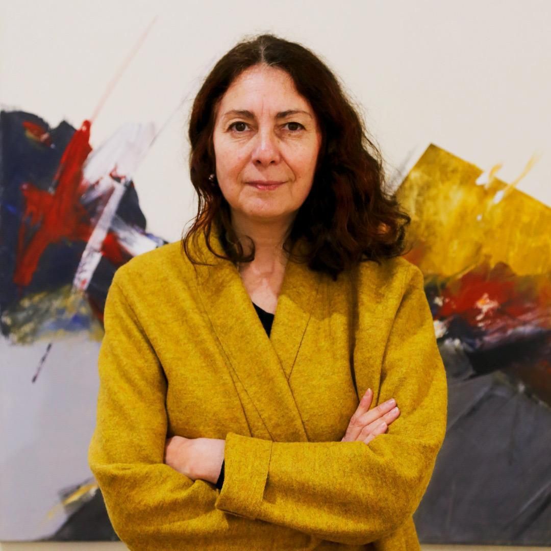 Headshot of a person with wavy brown hair and a mustard sweater, arms crossed.