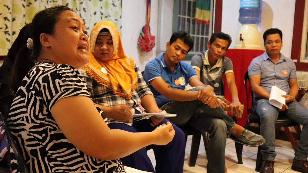 Four people in a half circle listening to a person wearing a patterned black and white shirt.