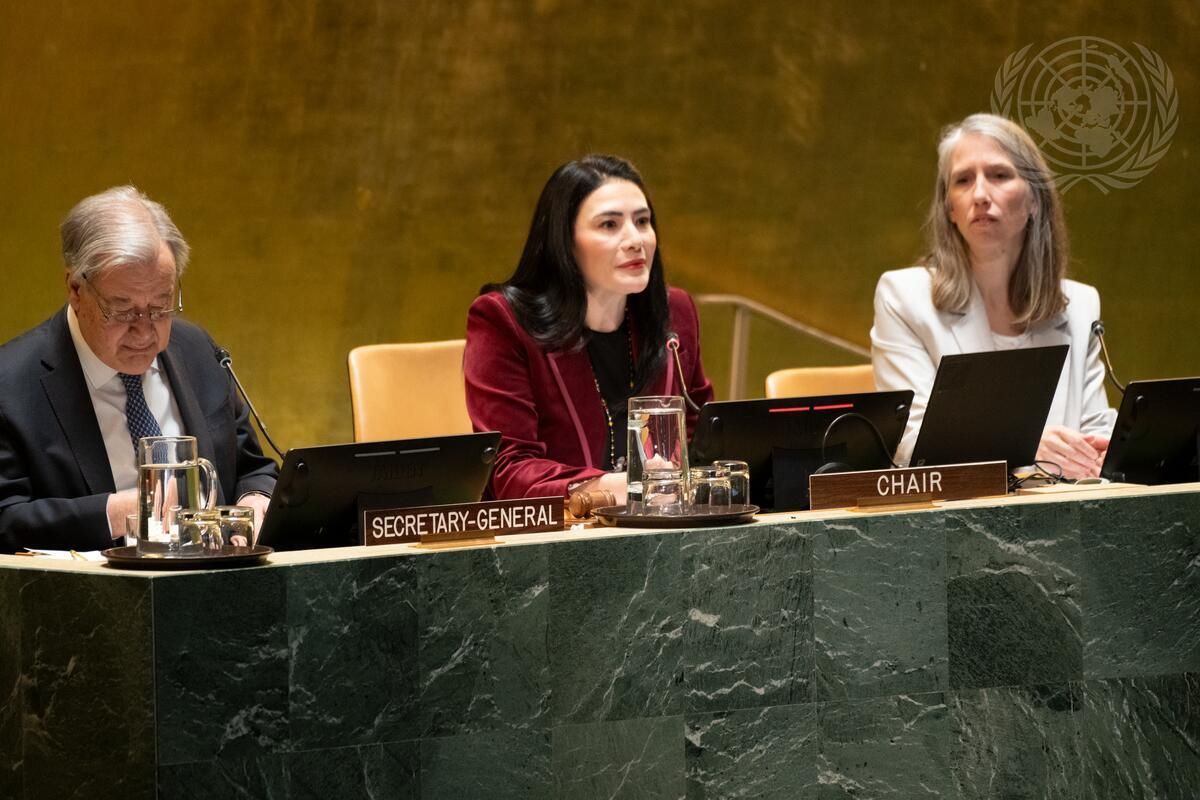 Three people sitting at a long table in the United Nations HQ conference room.