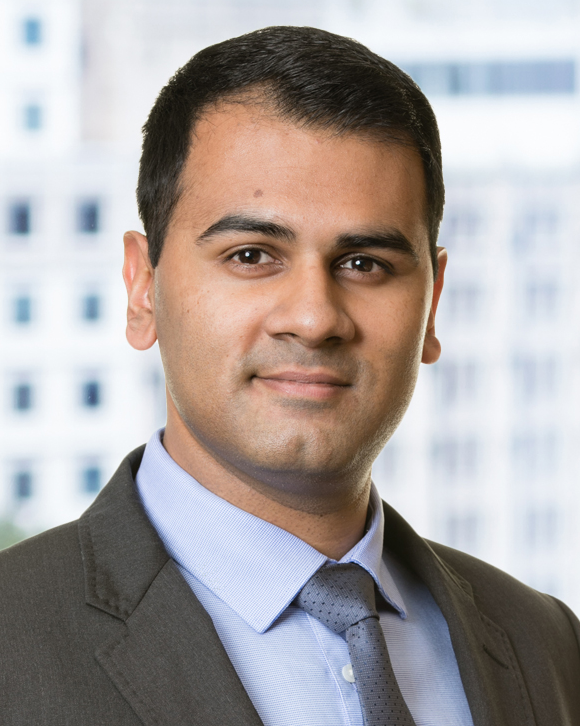 Headshot of a person wearing a dark suit jacket and blue collared shirt.